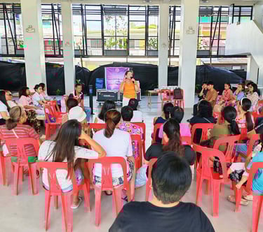 A community outreach seminar with a speaker addressing a group of local residents sitting in red chairs.