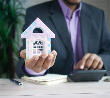 Agente immobiliare con in mano un modellino di casa appoggiato su una scrivania, accanto a una calco