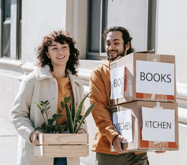 Couple walking together carrying moving boxes and house plants