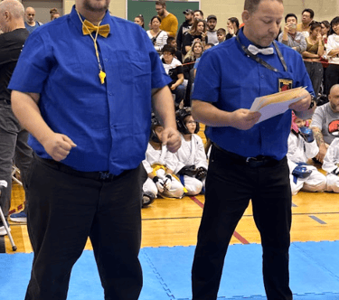 two men standing on a blue mat with a man in a blue shirt