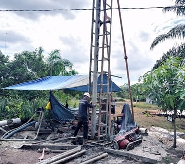 Worker operating a vertical drilling rig for water well construction at an outdoor site.