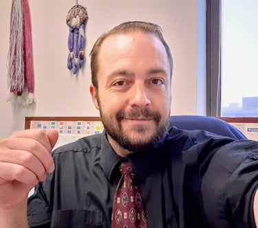 Professional man with a beard wearing a black dress shirt and patterned tie in an office.