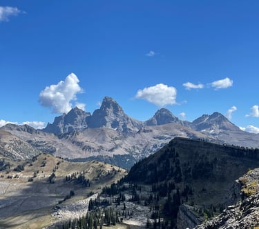 Panoramic view of the Grand Tetons mountain range with rugged peaks under a blue sky with fluffy clouds.