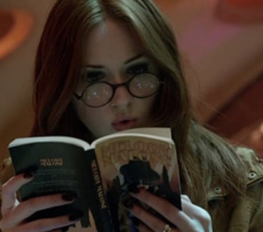 a woman in glasses and a jacket is reading a book