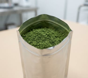 Macro shot of fine moringa powder packed inside a double-walled aluminum barrier bag, pristine clean-room environment, bright natural daylight, soft beige background