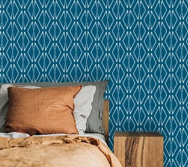 Bedroom corner with teal blue geometric diamond wallpaper, terracotta and gray pillows, and a wooden nightstand