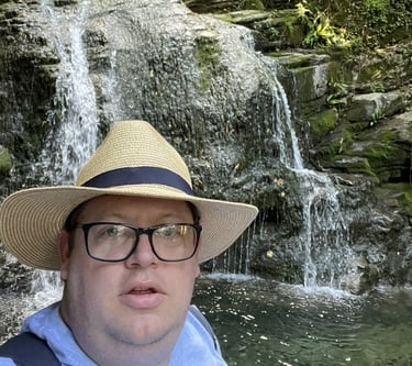 John Grimwood, operations director, in a Panama hat and dark glasses, in front of a waterfall.