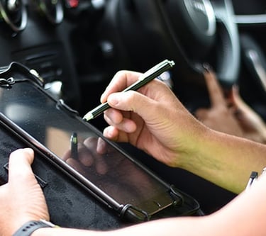 A driving examiner uses a stylus on a digital tablet to record results during a car driving test.