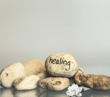 A zen stack of smooth river stones with 'healing' written on one, beside a white lotus flower.