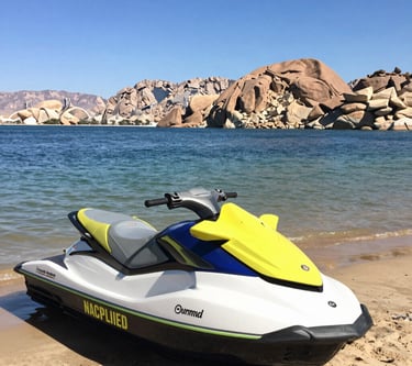 Three jet skis parked on a sandy beach near water.