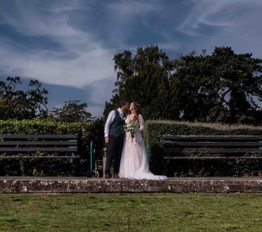 a bride and groom kissing on a bench in a park