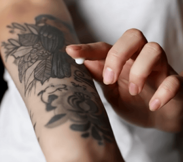 Aplicando crema hidratante de cuidado posterior para tatuajes sobre un nuevo tatuaje floral en negro