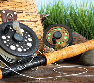 Fly fishing gear with a cork handle rod, reels, and flies next to a woven wicker creel basket.
