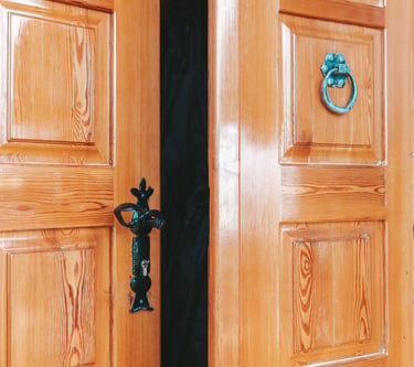 Polished wooden double doors slightly ajar with vintage metal hardware and a small circular window.