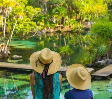 Dos viajeros con sombreros de paja contemplando un cenote de agua turquesa cristalina 