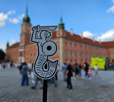 Magnes z Syrenką Warszawską na tle panoramy Placu Zamkowego