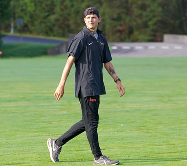 A smoldering photo of XC and Track and Field coach Justin Watson casually strolling across a field
