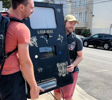 two men carrying a prototype photobooth made from wood