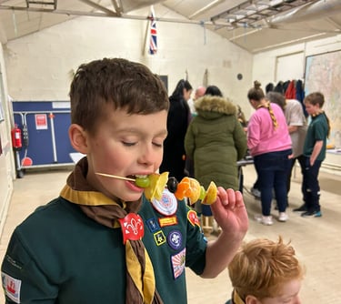 A cub from the 25th Allerton eats some fruit on a stick.