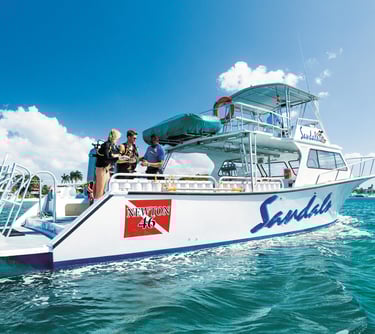 Scuba divers preparing for a dive on a Sandals luxury resort boat in tropical turquoise waters.
