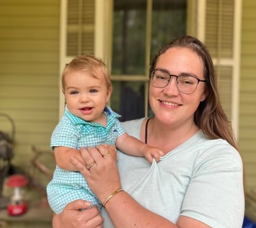a woman in glasses and a blue shirt holding a baby