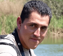 Headshot of Chiapas birding guide Eric Lopez Villanueva wearing binoculars with lake in background