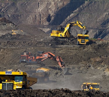 Heavy hydraulic excavators loading earth into large yellow haul trucks at a busy open-pit mining site.