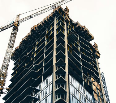 Low angle view of a modern skyscraper under construction with a yellow tower crane against a bright sky.