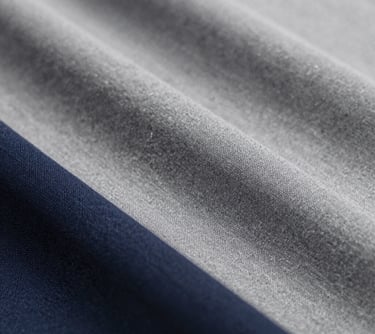 A macro shot of classic Pique and Single Jersey fabric samples in professional grey and navy shades, highlighting the texture and breathability required for fashion essentials.