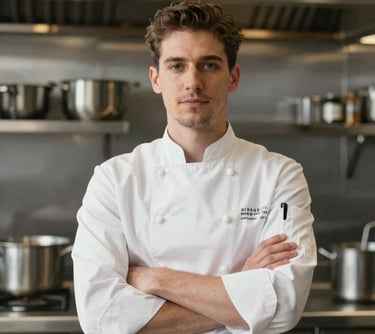 Professional portrait of a male chef in a clean white uniform and apron, arms crossed, sophisticated kitchen background with stainless steel and #4D6C58 details.