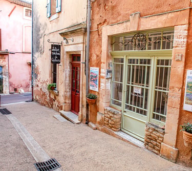 Quaint art gallery and studio along a narrow street with terracotta walls in Roussillon, France.