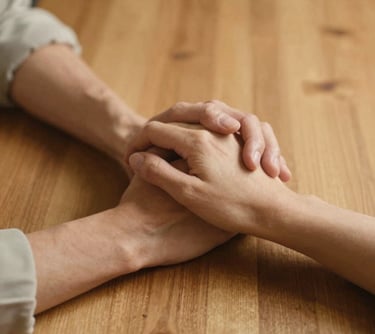 A close up of two people in a North American setting holding hands across a wooden table, emphasizing human touch and the bond of companionship. Warm gold lighting and a gentle, safe atmosphere.