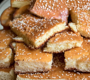 Slices of golden-brown semolina cake topped with white sesame seeds, a classic Middle Eastern dessert.