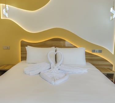 Luxury hotel bed with white swan towel art, warm LED backlighting, and modern yellow wall decor.