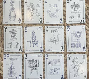 Twelve custom playing cards laid out on a woven surface, each featuring patent drawings on the face