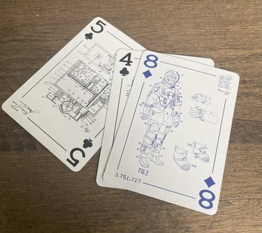 Three custom playing cards face up. The eight of diamonds is on top, showing a space suit drawing