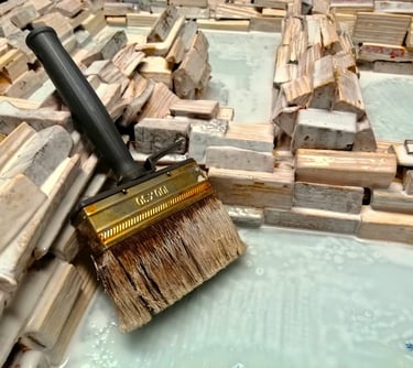 Foto eines großen Pinsels nach dem Einstreichen eines Spiegelrahmens aus unzähligen, naturbelassenen Holzscheiten