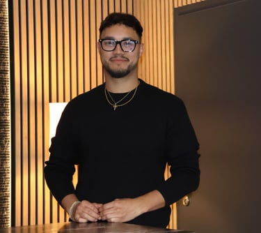 Professional man with glasses and black sweater standing against a modern wood slat wall.