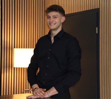 Smiling professional man in black dress shirt posing against a modern wood-slat wall background.