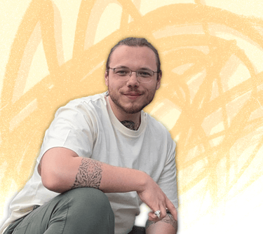 Smiling man with glasses and arm tattoos posing against an artistic yellow abstract background.