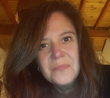 Close-up portrait of a woman with long brown hair inside a room with a rustic wooden ceiling.