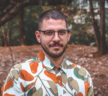 A man with glasses and a beard wearing a colorful floral print shirt outdoors in a park.