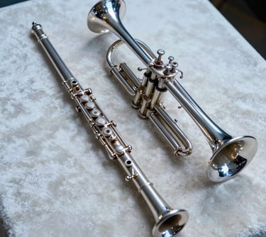 A detailed shot of a flute and a trumpet resting together on a pale off-white velvet cloth. The composition is clean and artistic, using soft steel blue lighting to create an accessible and professional mood.