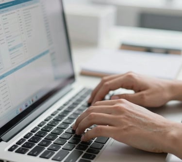 Close-up of hands on a laptop keyboard in a brightly lit open-plan office workspace, monitor displaying a data dashboard, clean cool white ambient light, shallow depth of field on the fingers, desk surface with notebook and pen visible at edge of frame