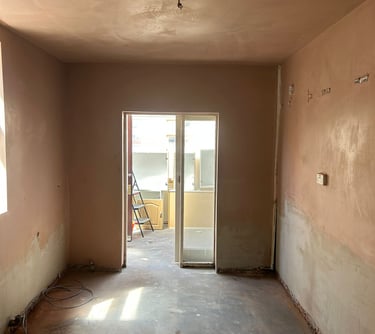 In the empty room under renovation, the walls have been freshly plastered and the concrete subfloor