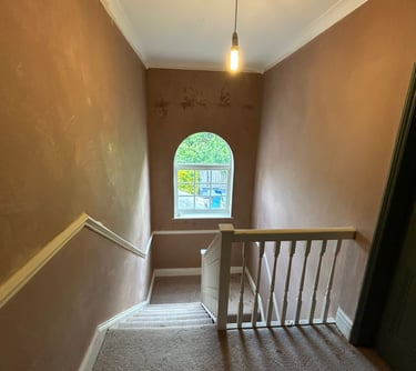 A carpeted staircase renovation with dusty pink walls, white banisters, and an arched window.