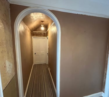 Freshly plastered brown walls and arched doorway in a home renovation hallway with striped carpet.