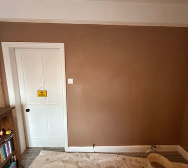 Freshly painted brown wall in a room with a white door and floor protected by a dust sheet.
