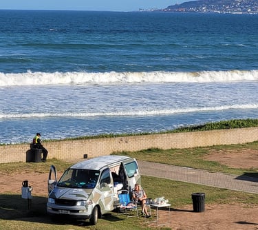 a van parked on the beach with people sitting in chairs