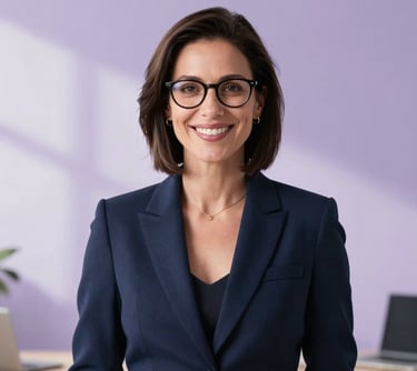Professional portrait of a woman in a smart casual navy blazer, smiling warmly. She has glasses and is set against a bright, minimalist office background with soft lavender purple shadows.